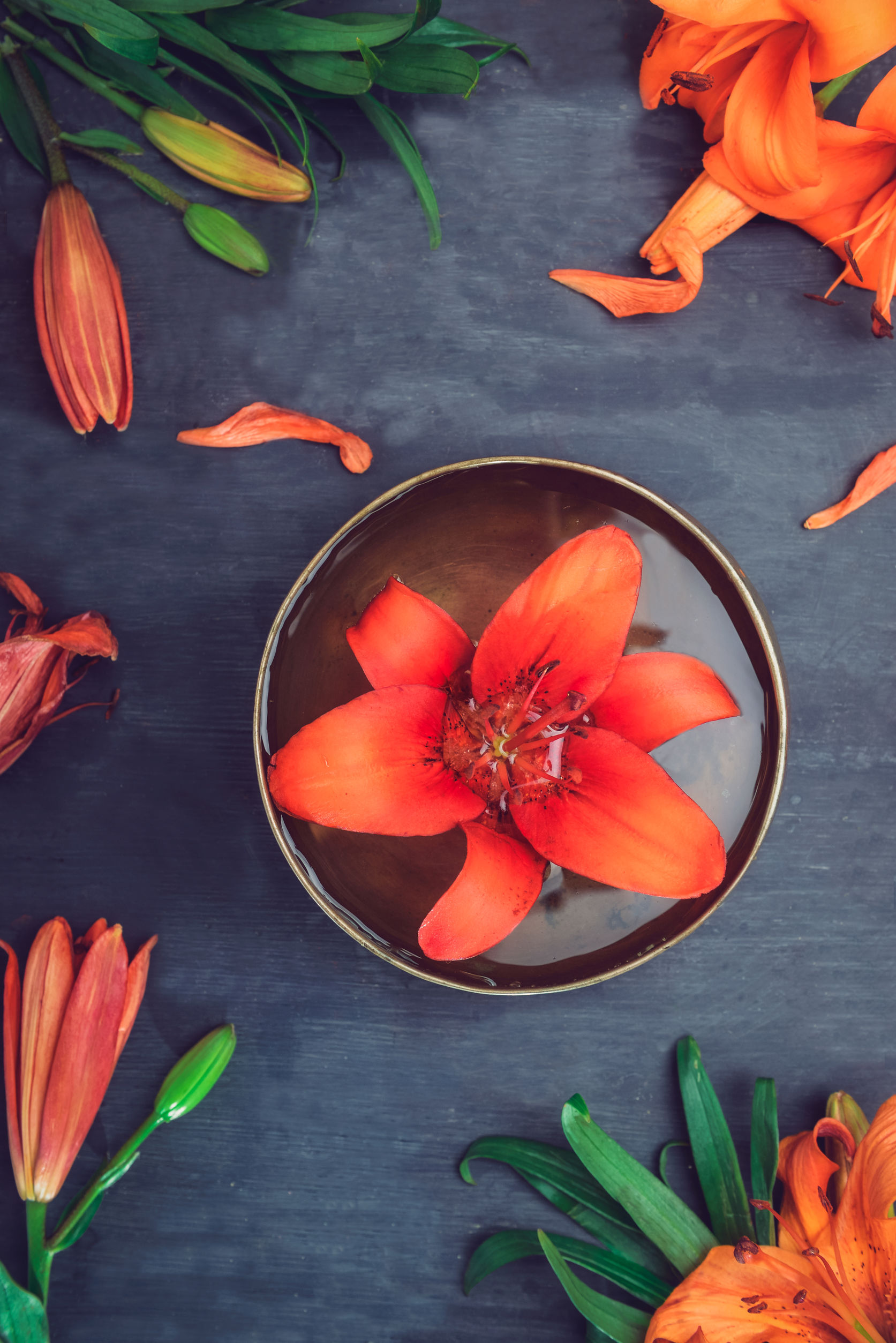 Tibetan singing bowl with floating lily inside. Burning candles, lily flowers and petals on the black wooden background. Meditation and Relax. Exotic massage, spa procedure. Selective focus